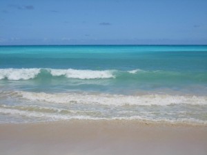 Turquoise ocean waves washing up against a sandy beach on a clear blue-sky day